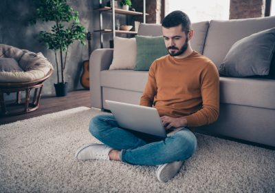 Portrait of concentrated focused man youth sit lotus position look read data statistics management denim jeans orange pullover sweater big light interior